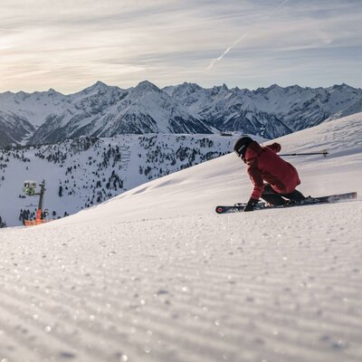 A skier on a groomed slope with the Zillertaler Alps and a ski lift in the background, indicating winter activities for guests of the Farm House.