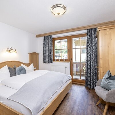 Double bedroom in the Farm House featuring a wooden bed, wardrobe, an armchair, and balcony access.