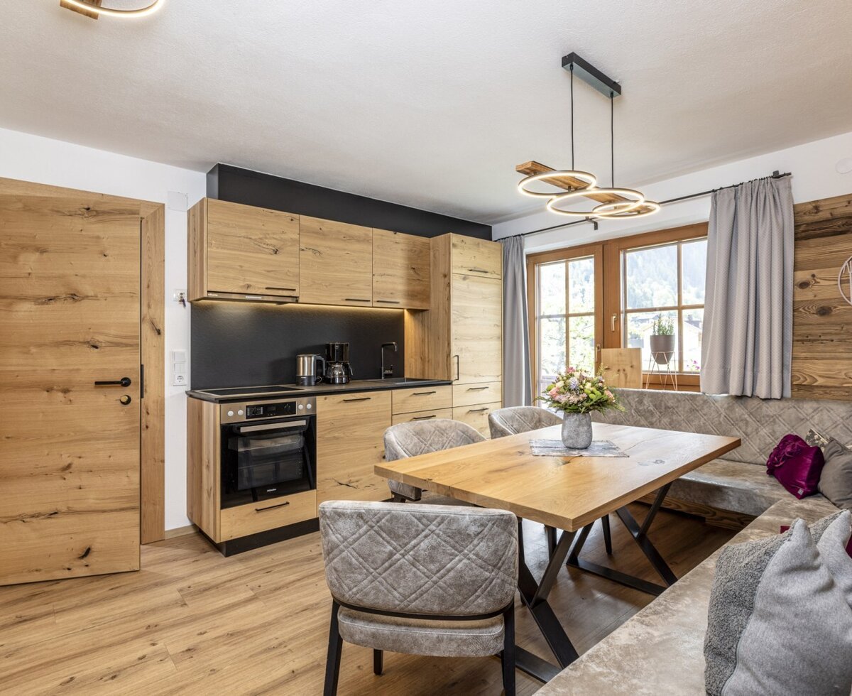 Combined kitchen and dining area in the Farm House, featuring modern wooden cabinets, an integrated oven, a large dining table, and U-shaped banquette seating by the window.