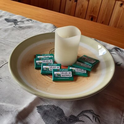 The dining table in the Alpine Hut, featuring a decorative candle and individually wrapped 'Urlaub am Bauernhof' chocolates.
