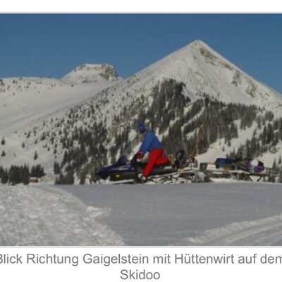 The Alpine Hut owner on a snowmobile against a backdrop of snowy mountains.