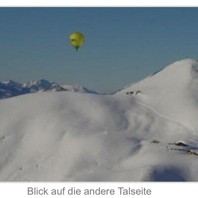 View of the snowy mountain landscape from the Alpine Hut, with a hot air balloon floating above distant peaks.