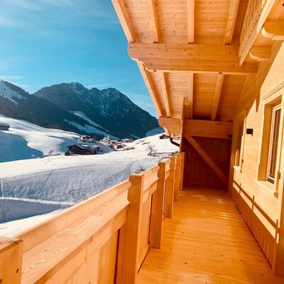 The wooden balcony of the farmhouse, overlooking snowy mountains and a village.