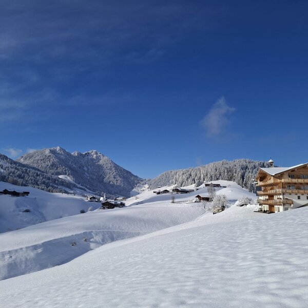 The farmhouse in a snowy mountain landscape with wooden balconies under a blue sky.
