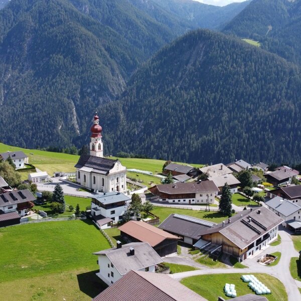 View of the village Asch with the farm, surrounded by green meadows and mountains, and a prominent church.