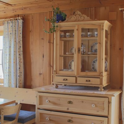 The farmhouse dining area features wooden paneling, a traditional display cabinet, and patterned curtains at the windows.