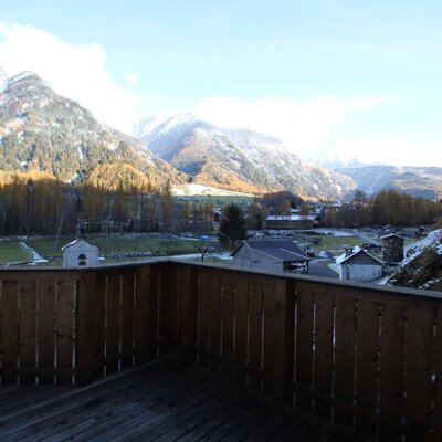 The Farm House balcony offers views of snow-dusted mountains, autumn trees, and a valley with buildings.