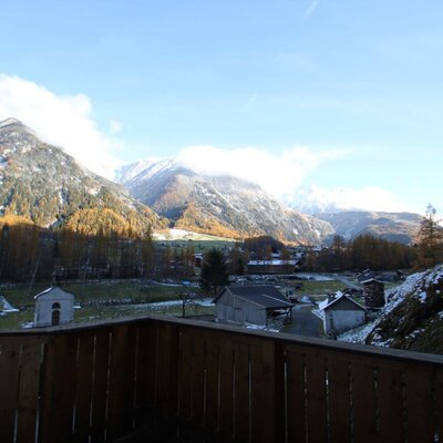 View from the Farm House balcony featuring snow-dusted mountains, a village in the valley, and trees with late autumn colors.