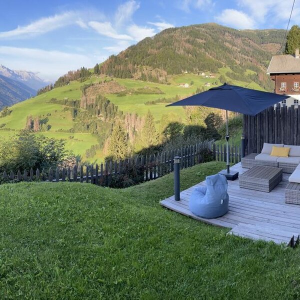 The farm house offers an outdoor wooden deck with sofa seating and an umbrella, providing views of the surrounding mountains and valley.