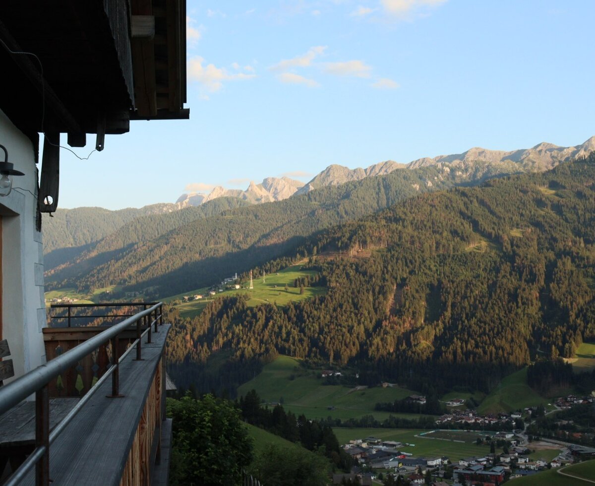 Balcony of the Farm House with a wooden bench, offering views of the forested mountains and the valley village.