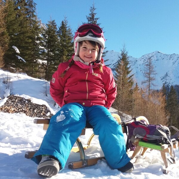 A child sitting on a sledge in a snowy landscape with mountains and evergreen trees, highlighting winter outdoor activities at the Farm House.