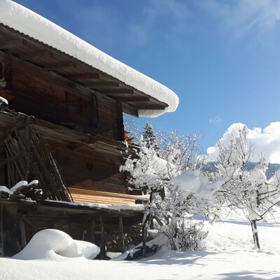 A traditional wooden farm building with a snow-covered roof on the Farm House property, set in a winter landscape under a blue sky.