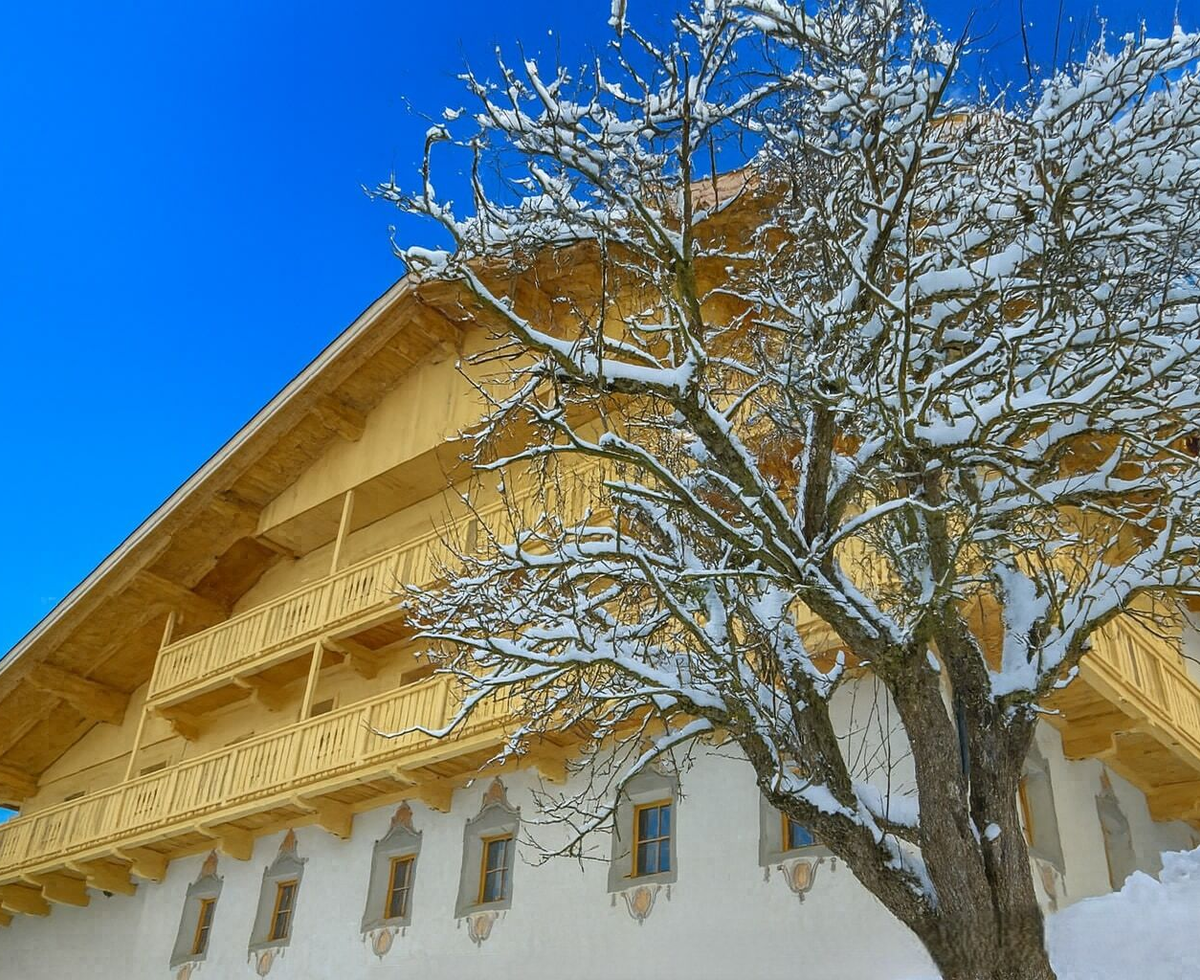 The snow-covered farmhouse featuring wooden balconies and a traditional facade in winter.