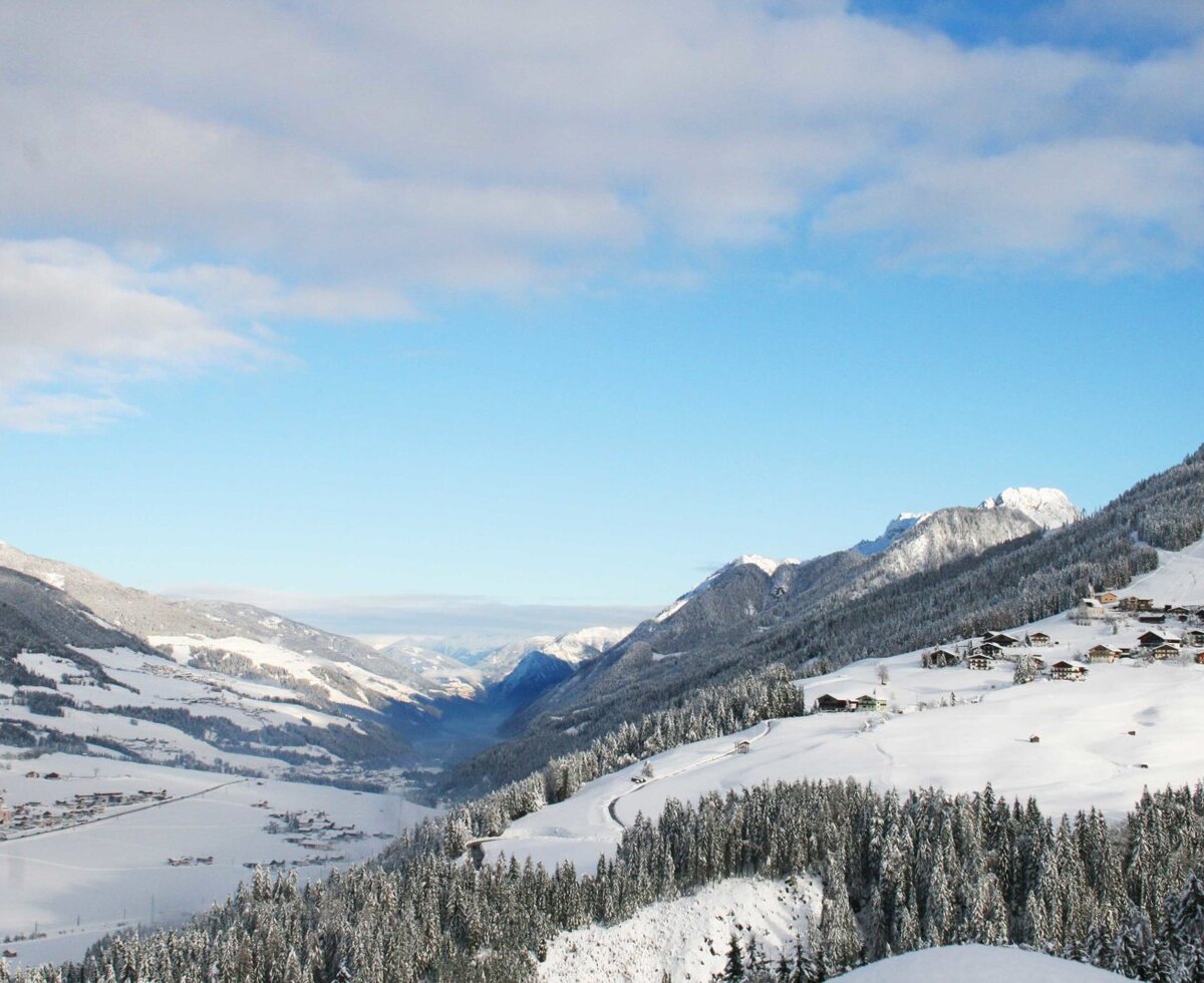View of the snow-covered valley and mountains, featuring a village and ski slope.