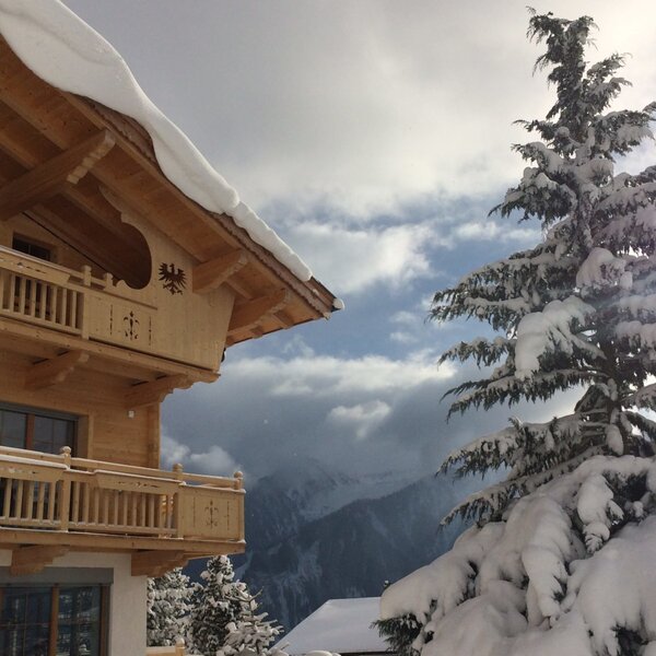 The Farm House exterior with traditional wooden balconies, snow-covered roof and railings, and a view of the surrounding snow-laden mountains. The Farm House exterior with traditional wooden balconies, snow-covered roof and railings, and a view of the surrounding snow-laden mountains.