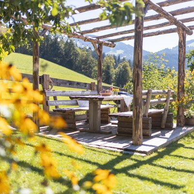 The covered outdoor seating area in the farmhouse garden with a wooden table and benches for al fresco dining.