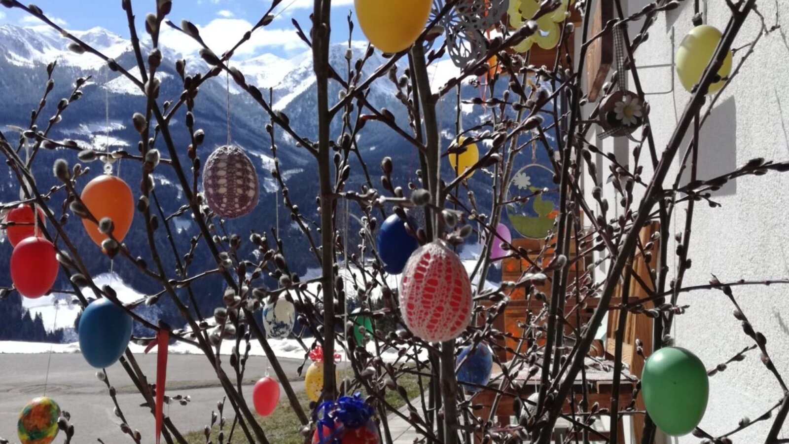 Pussy willow branches decorated with colorful Easter eggs at the farm house, featuring a view of snow-capped mountains.