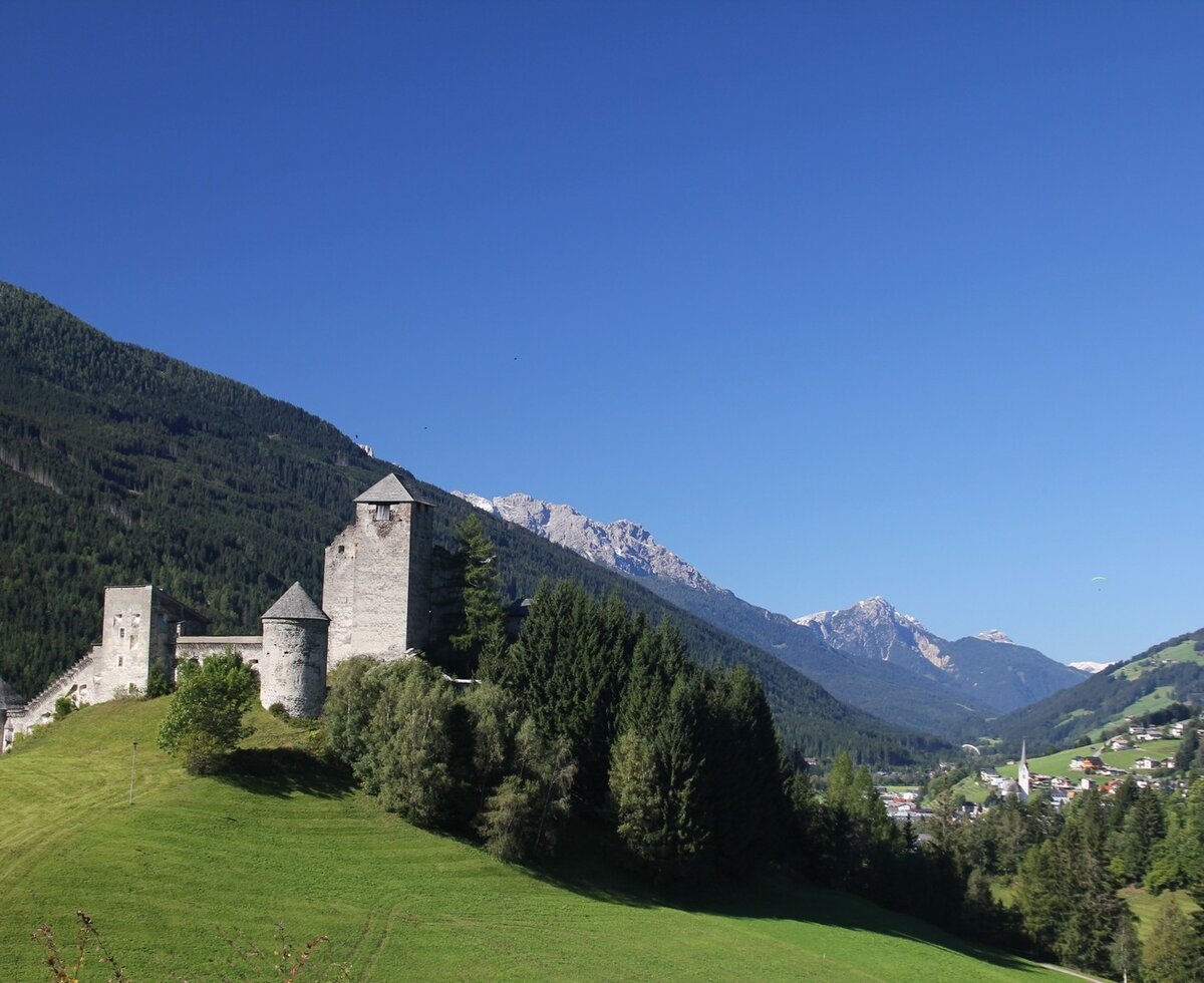 The Farm House is situated amidst green hills and mountains, offering views of a historic castle and a distant valley village.
