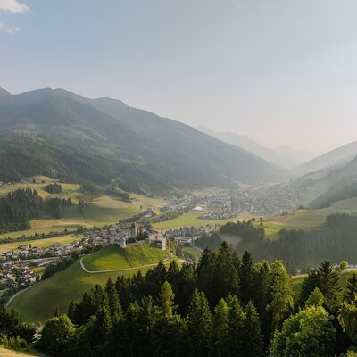 View of the valley with a town and a castle, surrounded by mountains and forests.