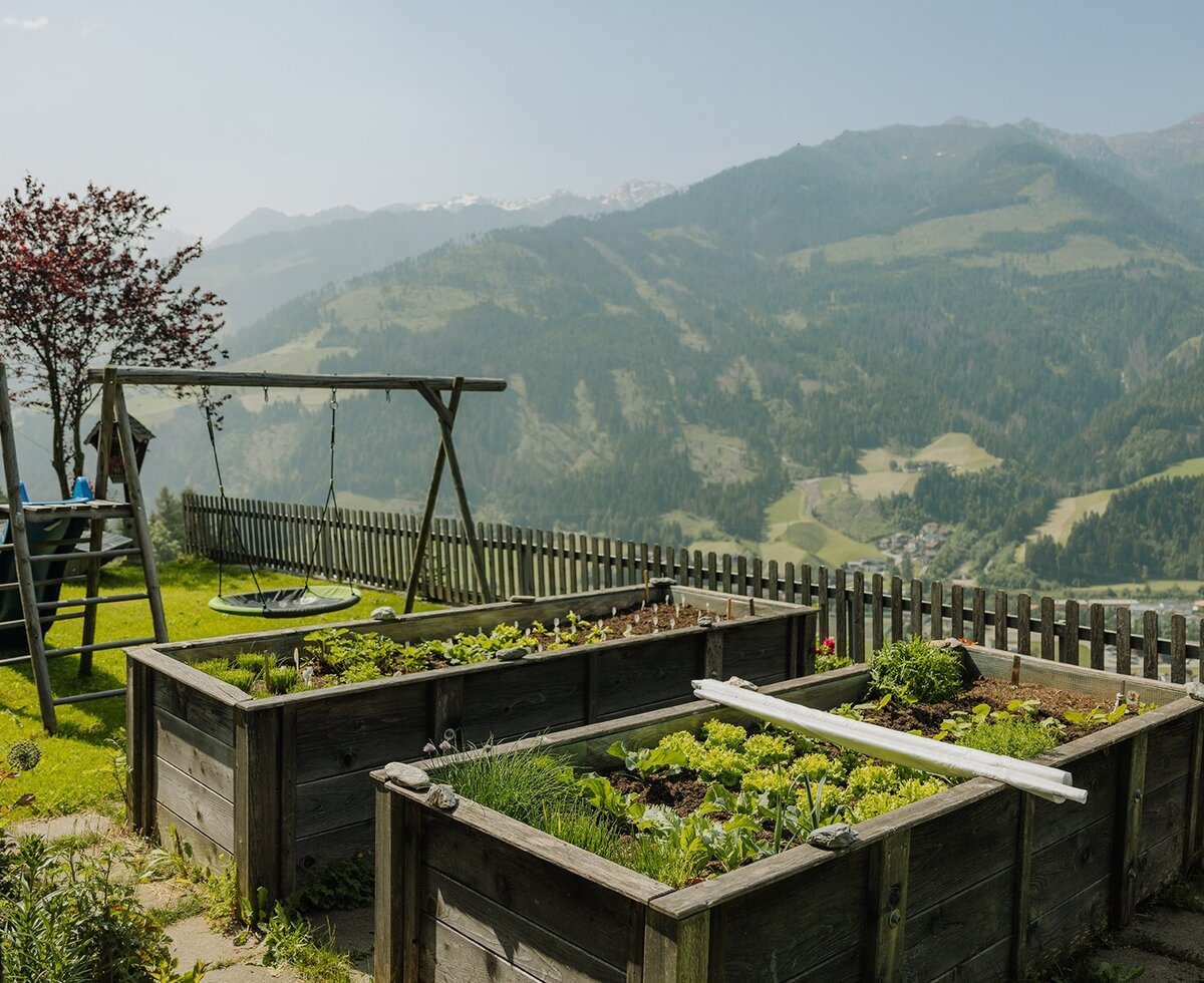 Raised garden beds with fresh plants and a children's playground at the farmhouse with mountain views.