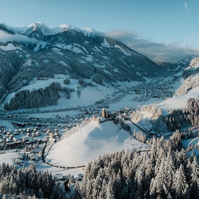 View of the snow-covered valley with a village and castle, surrounded by snowy mountains.