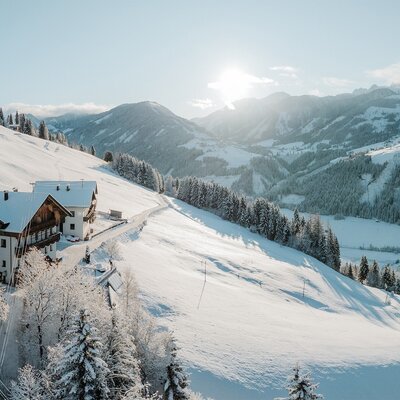 The farmhouse in a snowy mountain landscape under bright sunshine.