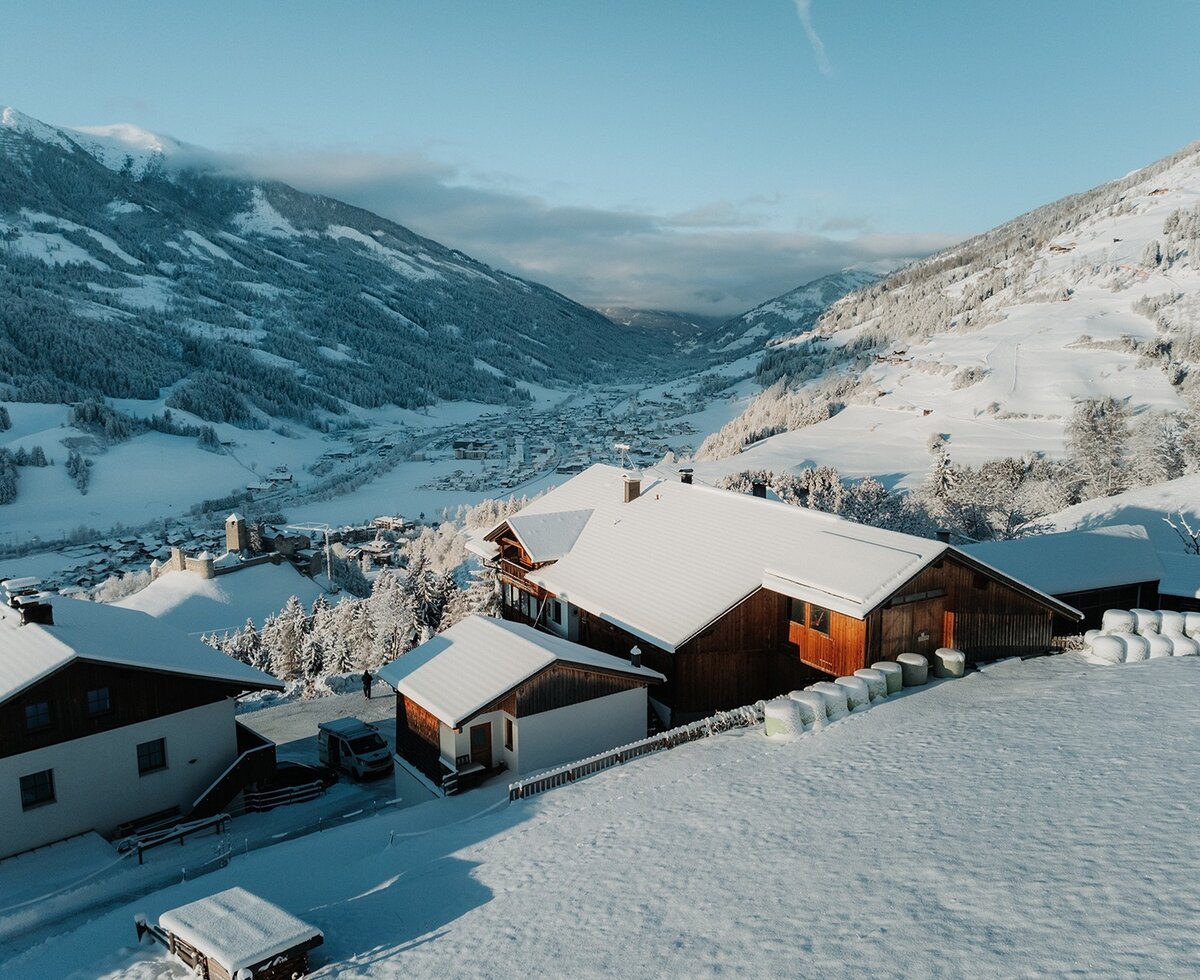 The farmhouse in winter, surrounded by snow and mountains, with a view of the valley.