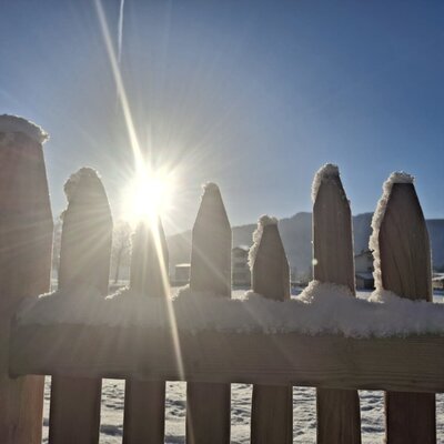 Sunny winter day on a farm with a snow-covered wooden fence.