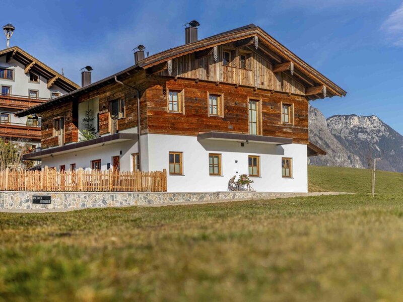 Exterior view of the Zuahaus building on the Bauernhof, featuring a traditional wooden facade, white ground floor, and mountain views.