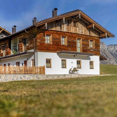 Exterior view of the Zuahaus building on the Bauernhof, featuring a traditional wooden facade, white ground floor, and mountain views.