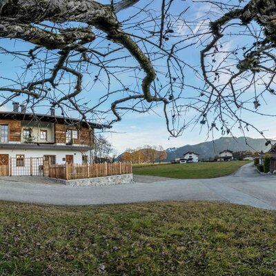 Exterior view of the 'Zuahaus' farmhouse with a white facade, wooden cladding, and the surrounding mountain landscape.