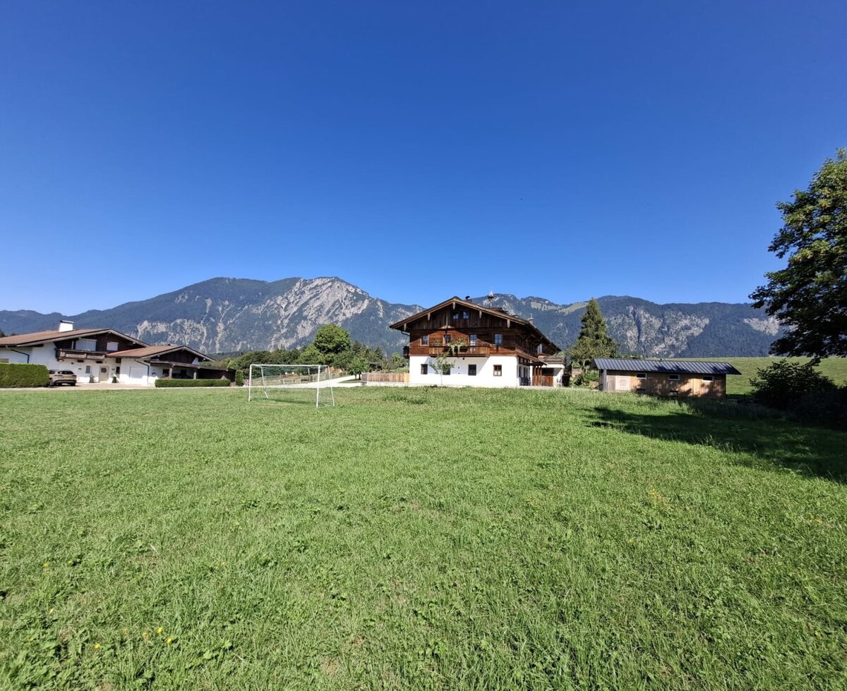 The inviting farmhouse surrounded by a spacious green meadow with a soccer goal and scenic mountain views in the background.