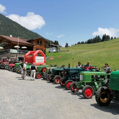 A line of vintage tractors parked in front of the inviting farmhouse, surrounded by lush green meadows and a bouncy castle.