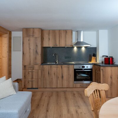 Modern kitchen in the Ap­par­te­ments with wooden cabinets, a sink, stove, and oven, open to the living area.