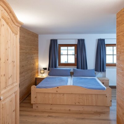 Bedroom in the Ap­par­te­ments with a wooden double bed, wooden wardrobe, and two windows.