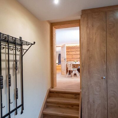 Entrance area of the Ap­par­te­ments featuring a wooden staircase, coat rack, and built-in wardrobe, with a view into the living area.