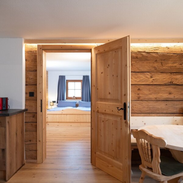 Kitchen and dining area of the Ap­par­te­ments, featuring wooden furnishings and access to a bedroom.