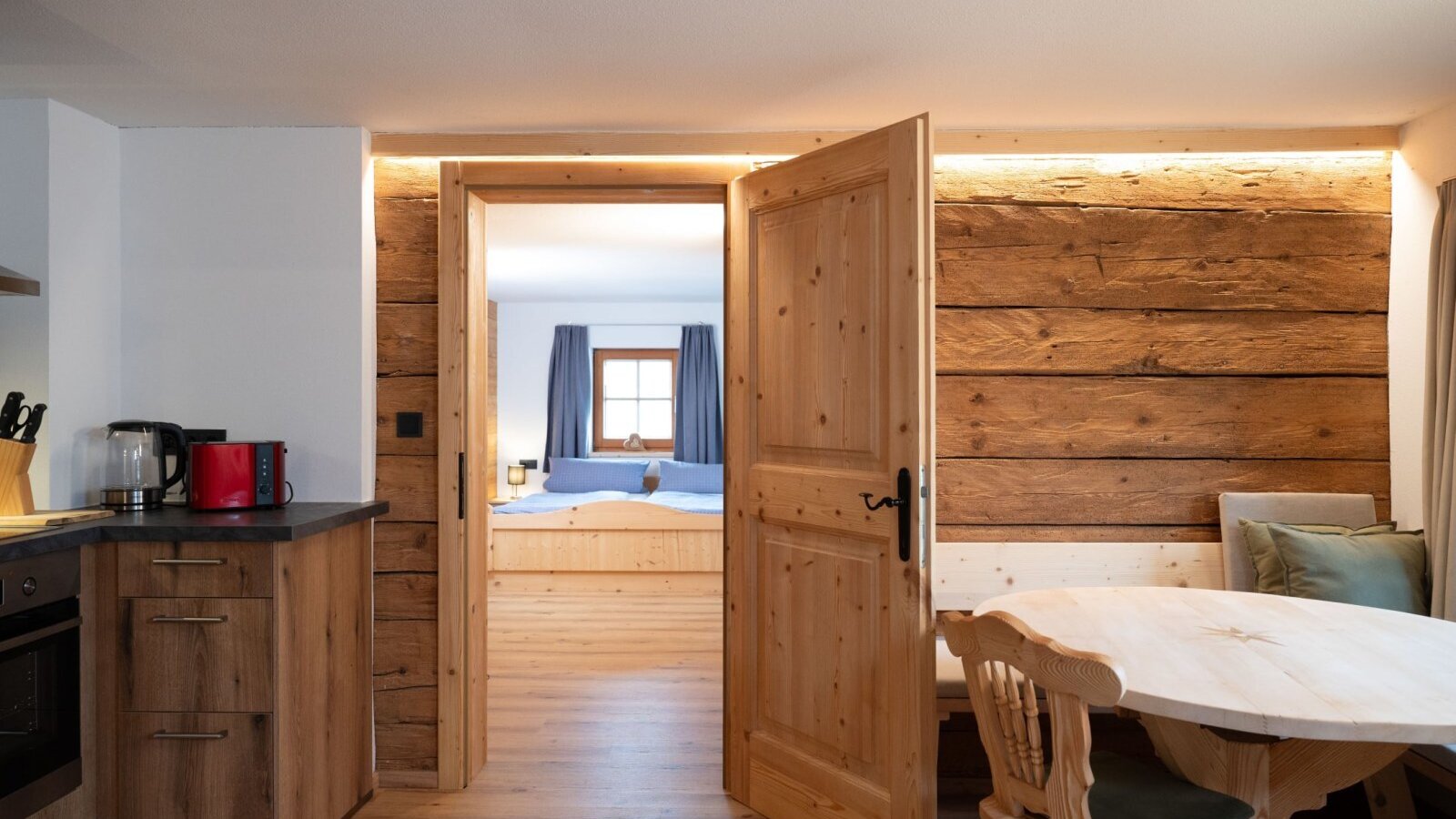 Kitchen and dining area of the Ap­par­te­ments, featuring wooden furnishings and access to a bedroom.