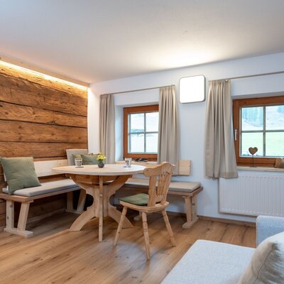 Living and dining area of the apartment with a wooden table, corner seating, and two windows.