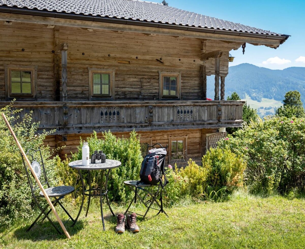 The farmhouse's idyllic exterior featuring a cozy outdoor seating area on the green lawn with scenic mountain views.