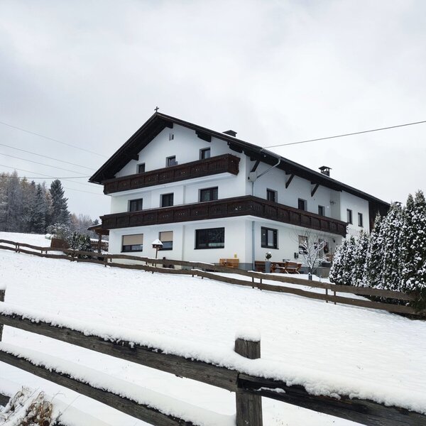 Exterior view of the farmhouse in winter, surrounded by snow and a wooden fence.