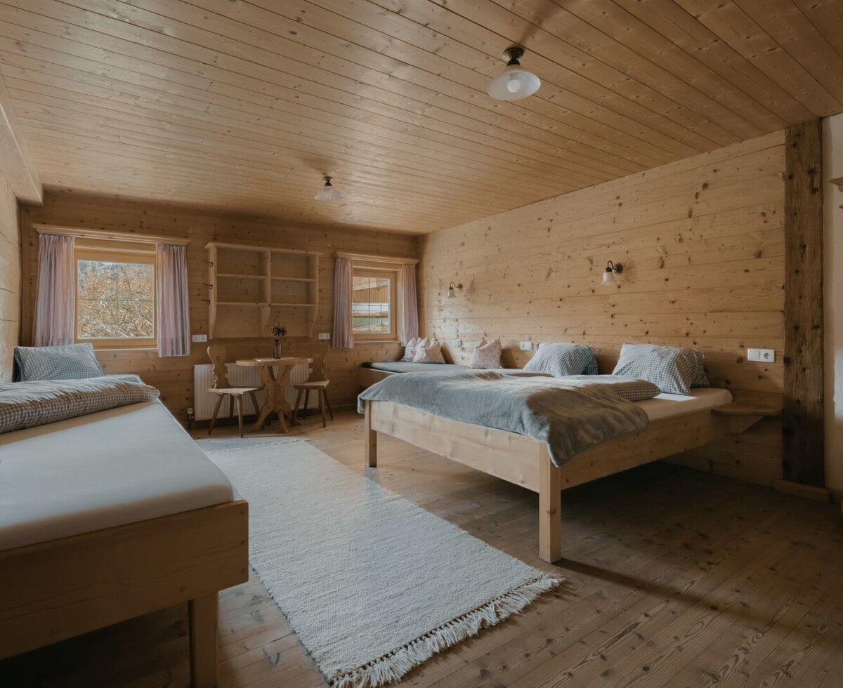 Bedroom of the Ferienwohnung with a double bed, single bed, wooden walls, and a small dining area.