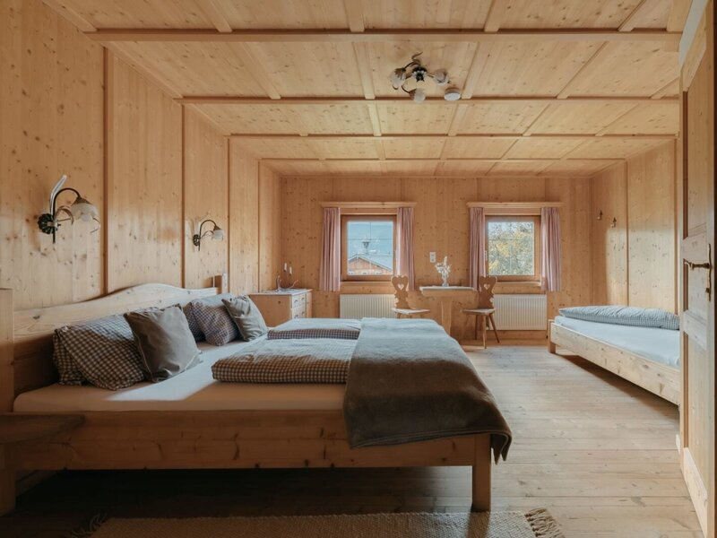 Bedroom of the Ferienwohnung with a double bed, a single bed, wood paneling, and a small table with chairs.
