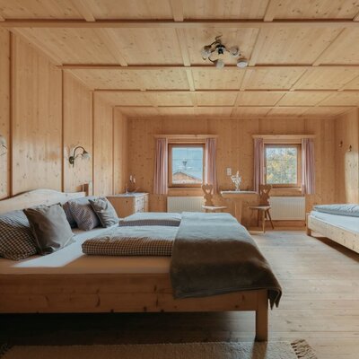 Bedroom of the Ferienwohnung with a double bed, a single bed, wood paneling, and a small table with chairs.