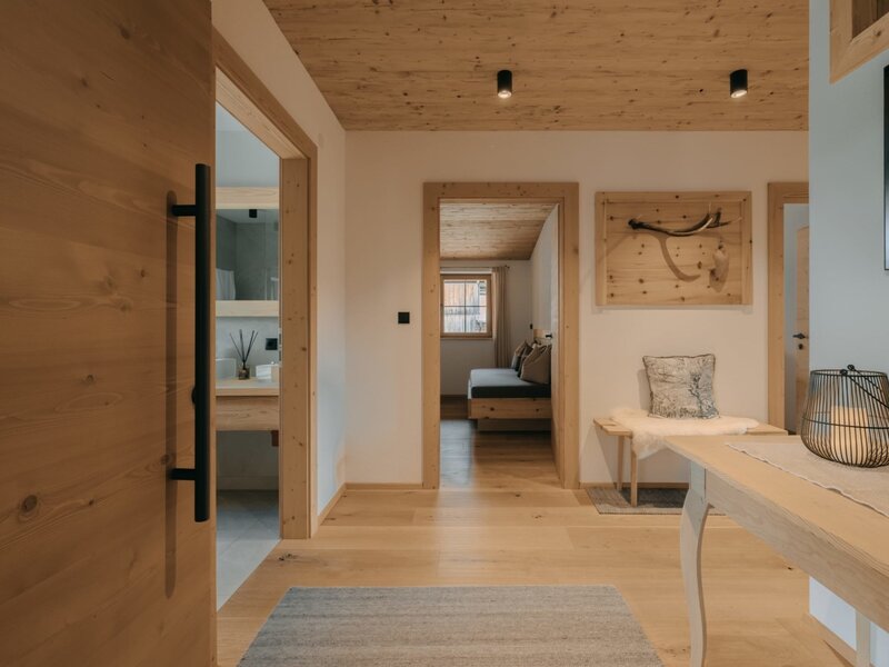 The entrance area of the Ferienwohnung, featuring a wooden floor, wooden ceiling, a bench, and access to other rooms.