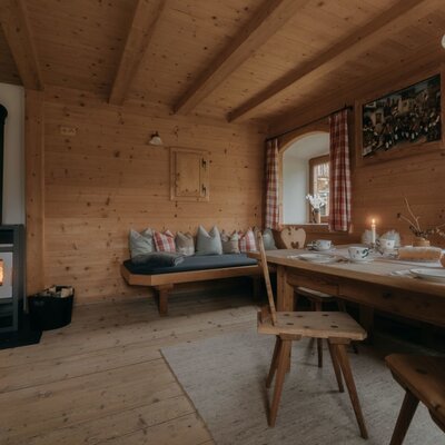 Dining area of the Ferienwohnung with a wooden table, bench seating, and a wood-burning stove.