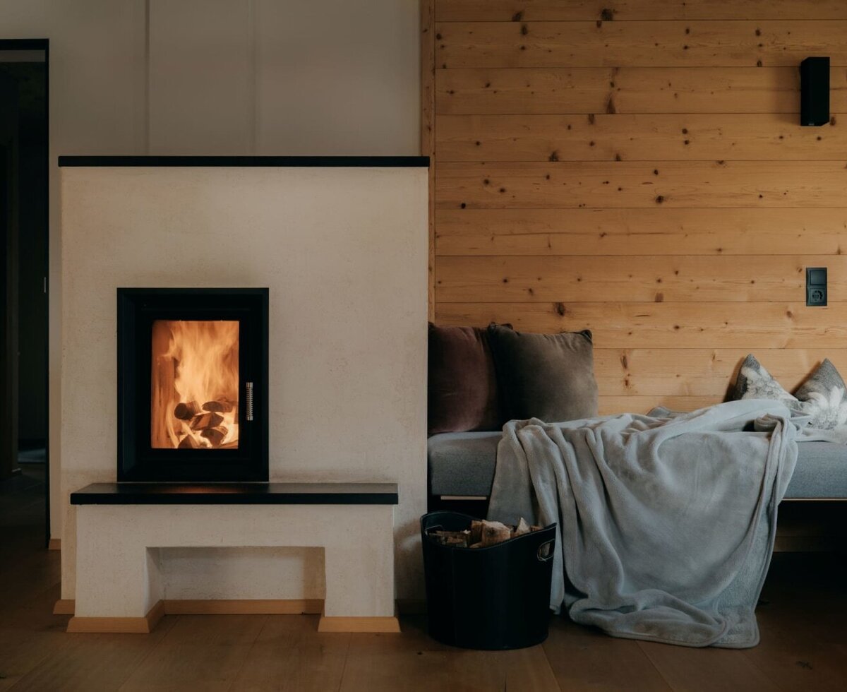 Fireplace in the apartment with a burning fire, a bench, and a basket of firewood.