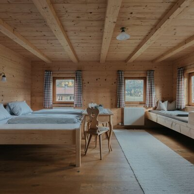 Bedroom in the holiday apartment with wooden walls, two single beds, and a wooden bench for additional sleeping.