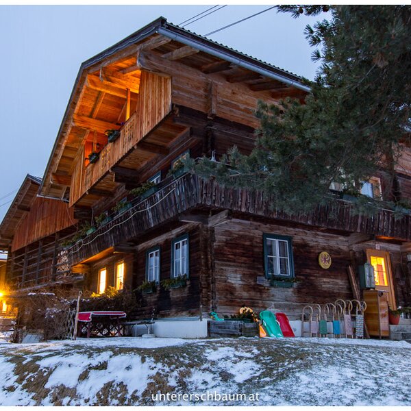 The wooden Farm House exterior, featuring illuminated windows and balconies in a snowy winter setting.