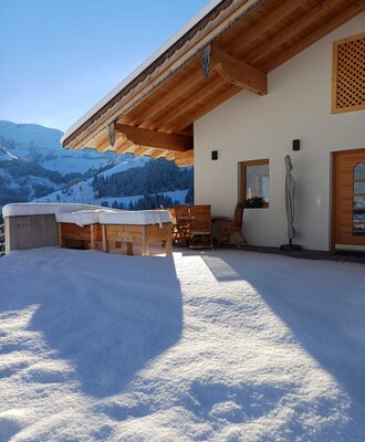 The snowy terrace of the farmhouse, featuring outdoor furniture and a view of the winter mountain landscape.